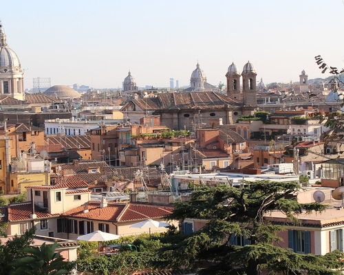 Blick über die Dächer der römischen Altstadt mit mehreren Kirchtürmen und Kuppeln, darunter die markante Kuppel der Kirche Sant’Agnese in Agone, eingerahmt von Bäumen.